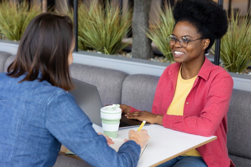 Young and pretty African American woman chatting with friend or colleague in coffee shop